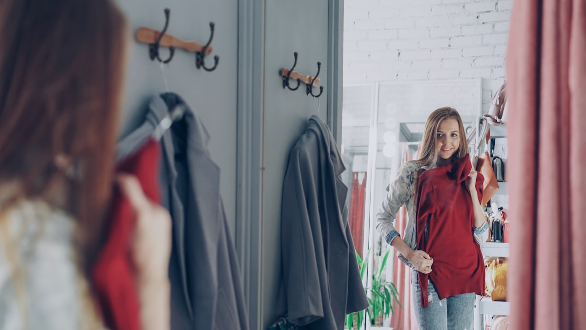 Someone trying on a red top in front of a fitting-room mirror