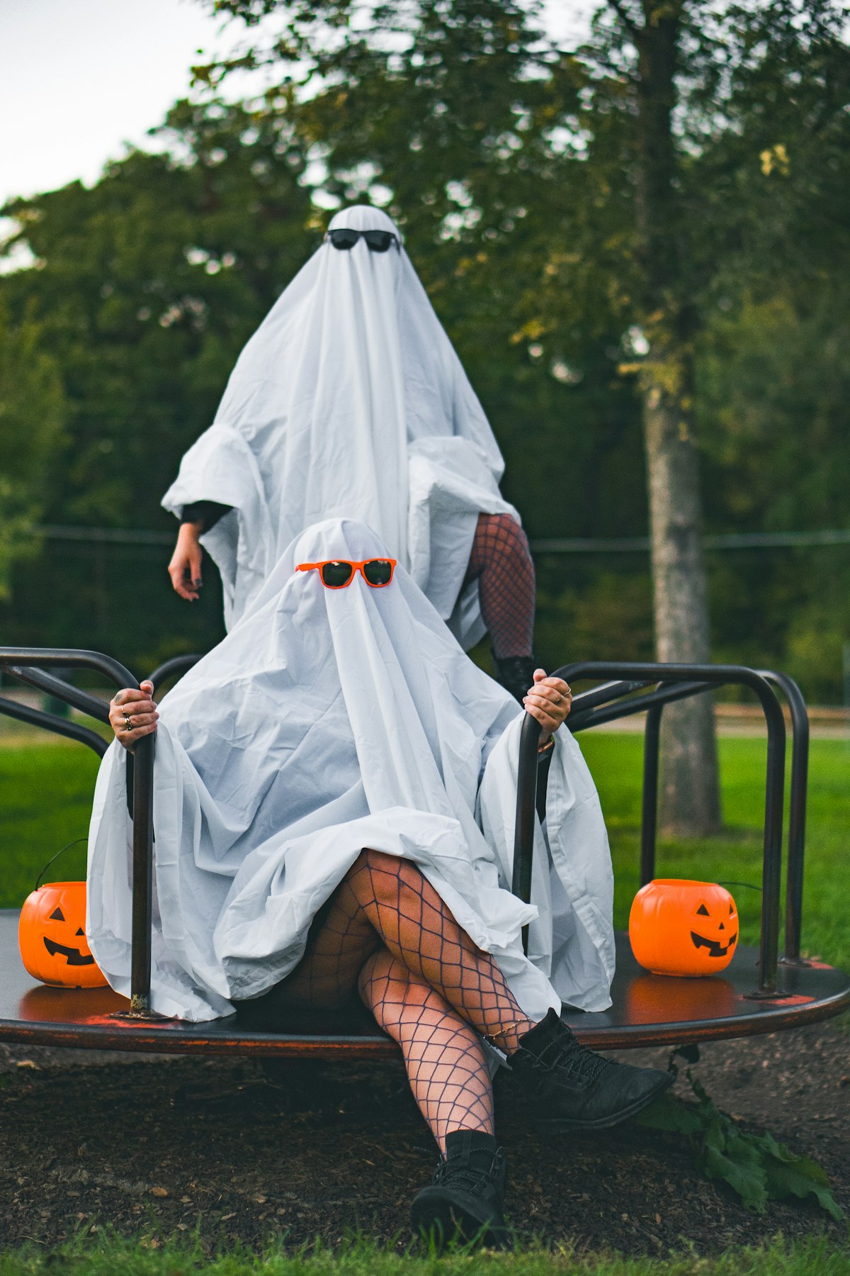 Two people dressed as ghosts in white sheets and sunglasses, beside carved pumpkins