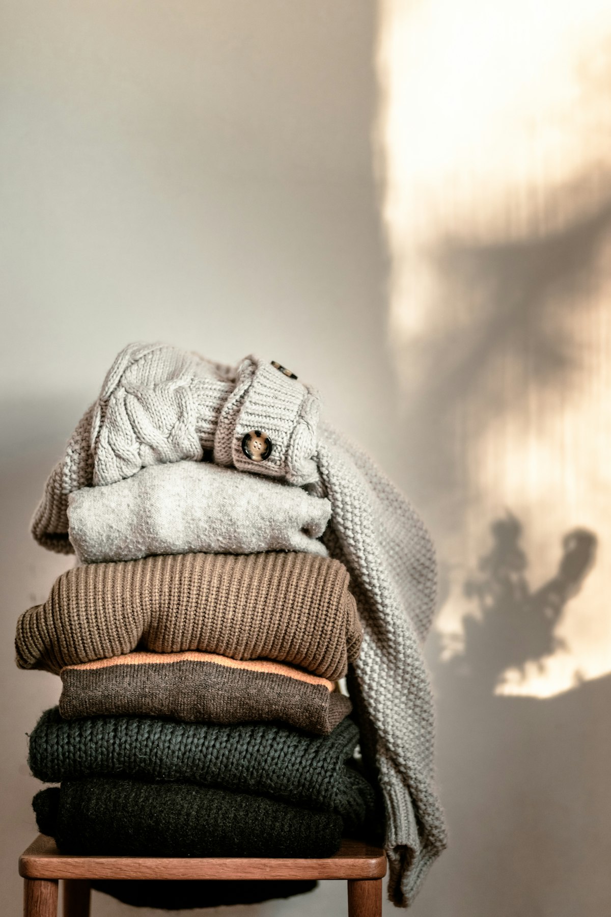 A stack of folded knitted jumpers on a wooden chair