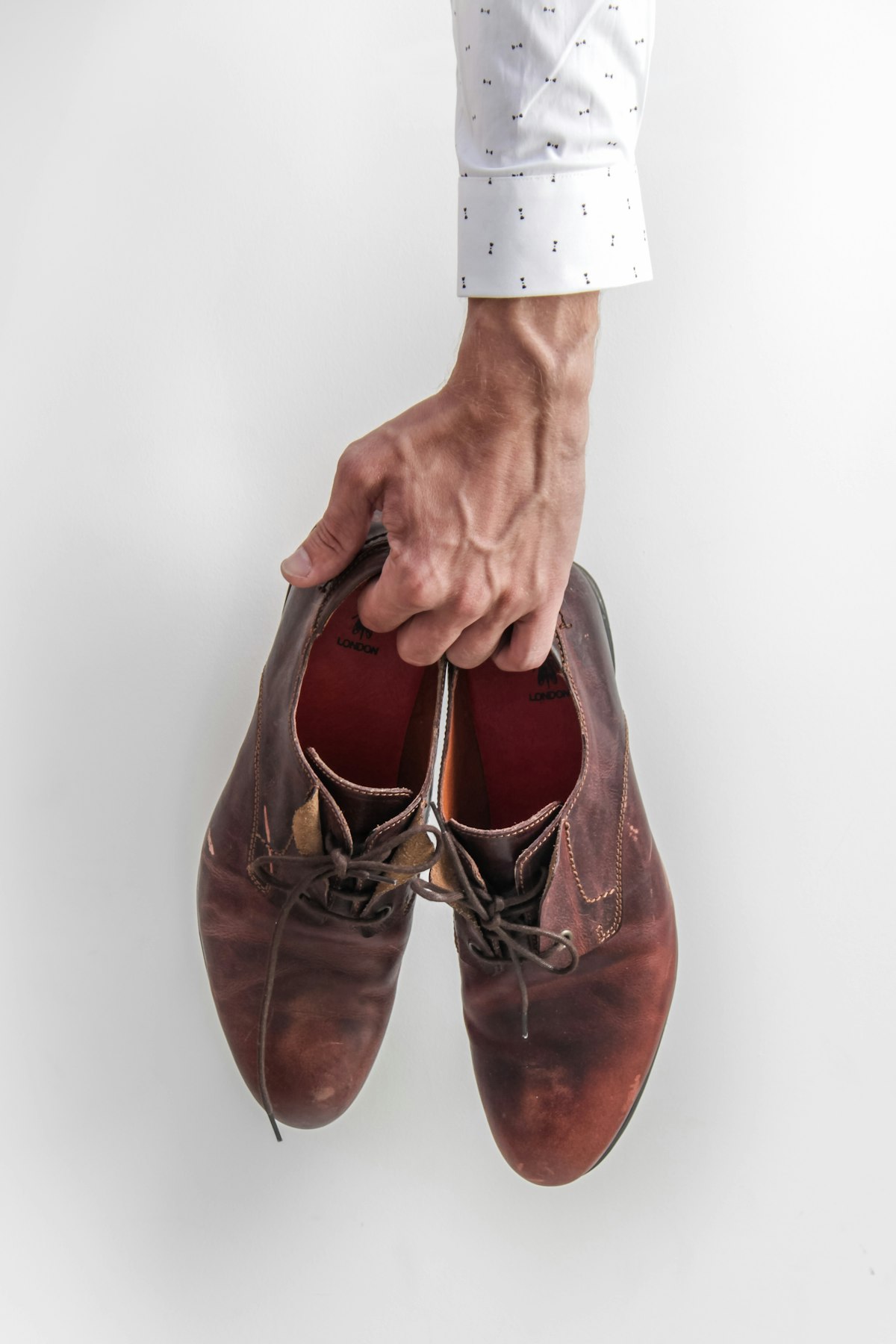 A pair of brown leather shoes held up for inspection