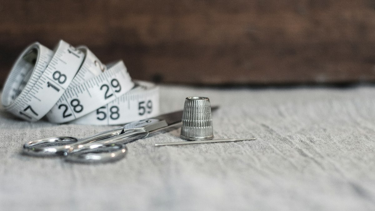 A tape measure, scissors, a thimble and a needle on linen