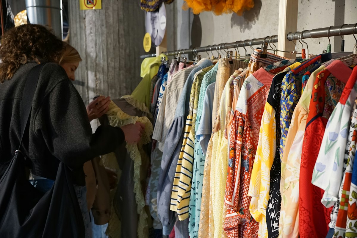 A person browsing a rail of colourful second-hand blouses at a clothing swap