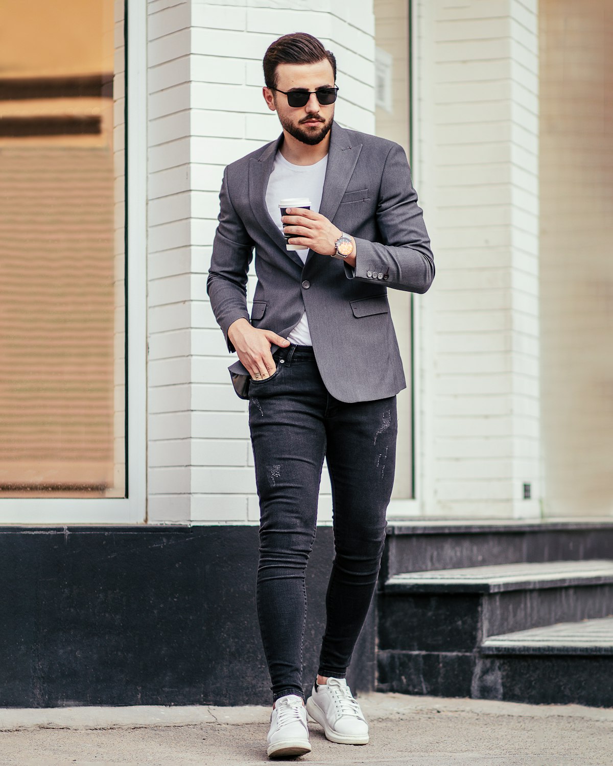 A person in a grey blazer, white t-shirt, dark jeans and white trainers
